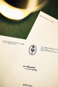 two envelopes sitting next to each other on top of a green table with a gold spoon in the background