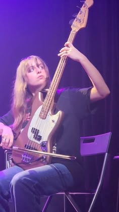 a woman sitting in a chair with a bass guitar on her lap and looking up at the sky