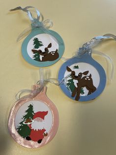 three christmas ornaments hanging on a table with ribbons and tags in the shape of reindeers