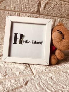 a teddy bear sitting next to a white frame with the letter h written on it