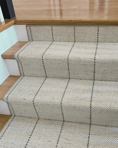 a cat sitting on top of a carpeted stair case next to a wooden handrail