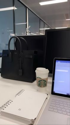 a laptop computer sitting on top of a desk next to a cup of coffee and a bag