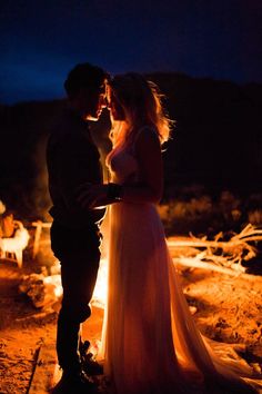 a man and woman standing next to each other in front of a campfire at night