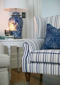 a blue and white striped chair sitting next to a table with a lamp on it