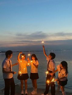 a group of people standing on top of a beach holding sparklers