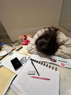 a person laying on top of a table covered in papers and pencils next to a cell phone