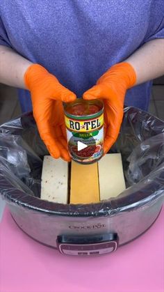 a person wearing orange rubber gloves holding a jar of food