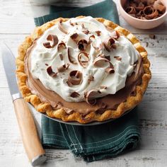 a chocolate pie with whipped cream on top sitting on a green napkin next to a knife