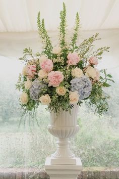 a vase filled with lots of flowers on top of a white table next to a window