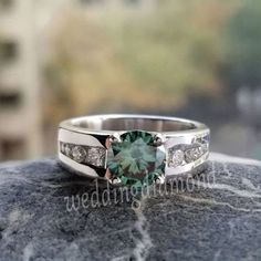 an engagement ring with a green stone surrounded by white diamonds on top of a rock