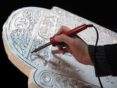 a person holding a pen and drawing on a large piece of paper with intricate designs