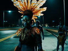 some people are walking down the street at night wearing costumes with feathers on their head