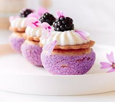 three desserts with white frosting and blackberries on top sit on a plate