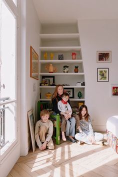 a woman and two children sitting on the floor in front of a bookshelf