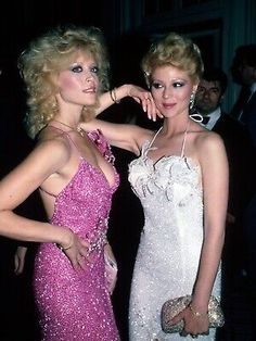 two women standing next to each other in formal wear at an event, one wearing a pink dress and the other white