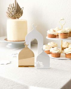 cupcakes and cakes on a table in front of a cake stand with a mosque cutout