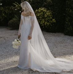 a woman in a wedding dress holding a bouquet and looking at the back of her gown