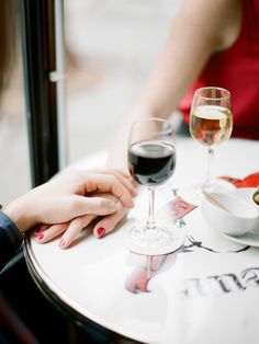 two people sitting at a table holding hands with wine glasses in front of them on the table