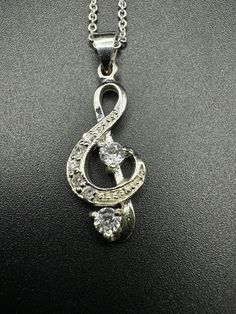 a musical note pendant with crystal stones in the center on a black surface, hanging from a silver chain