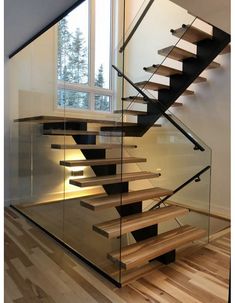 a glass stair case with wooden steps in front of a window and wood flooring