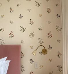 a pink bed sitting next to a white wall with flowers on it and a gold headboard