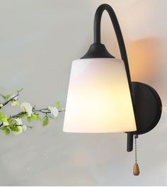 a wall light with a white shade hanging from it's side and flowers in the background