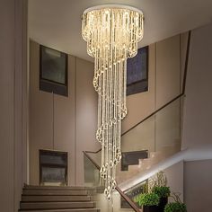 an elegant chandelier hanging from the ceiling in a foyer with stairs and potted plants