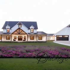 a large white house sitting on top of a lush green field next to purple flowers