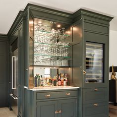 a green cabinet with wine glasses and liquor bottles on the top, in a kitchen