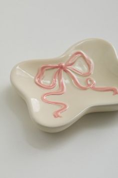 a white and pink ceramic dish with a bow on the front, sitting on a table