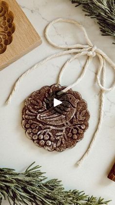 an ornament is hanging from a string on a table next to some pine branches