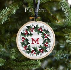 a cross stitch christmas ornament hanging on a tree branch with the word merry written in red and green