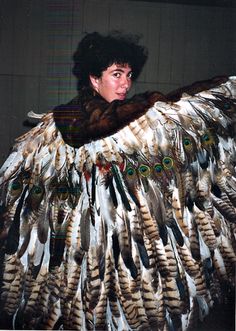 a woman with feathers on her body and fur collar standing in front of a wall