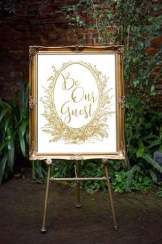 an easel with a sign that says be our guest in gold lettering on it