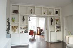 a living room filled with lots of white furniture and bookshelves on the wall