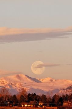 the moon is setting over the mountains in the evening sky, with snow on them