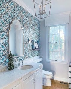 a bathroom with blue and white wallpaper has a chandelier over the sink