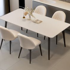 a white dining table with four chairs and a vase filled with flowers on the counter