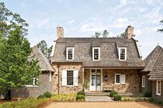 a stone house with white shutters on the front and side windows, surrounded by trees