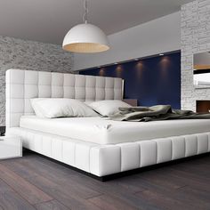 a large white bed sitting on top of a hard wood floored floor next to a brick wall