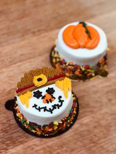 two decorated cakes sitting on top of a wooden table next to oranges and pumpkins