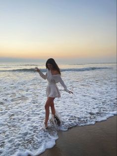 a woman standing on top of a sandy beach next to the ocean