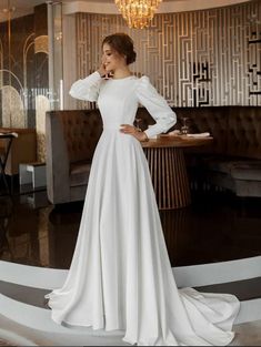 a woman standing in front of a couch wearing a white wedding dress with long sleeves