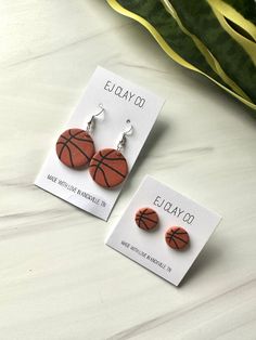 two earrings with basketballs on them are sitting next to a plant and some cards