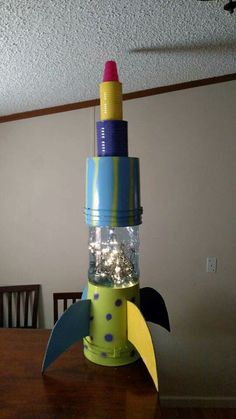 a rocket ship made out of plastic bottles on top of a wooden table next to a ceiling fan