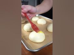 a person using a red spatula to make doughnuts on a baking sheet