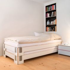 a white bed sitting on top of a hard wood floor next to a book shelf