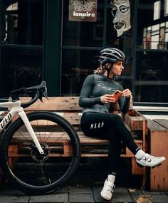 a woman sitting on a wooden bench next to a bike and looking at her phone