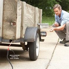 a man kneeling down next to a wooden box on the side of a road with a hose connected to it