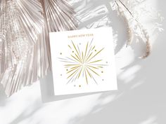 a white card with gold foil stars on it next to some palm leaves and plants